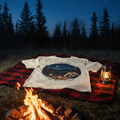 Star Gazin' tee laid on a plaid blanket beside a campfire under a twilight sky with the first stars